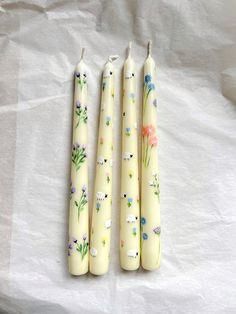 three candles with flowers painted on them sitting next to each other in front of a white sheet