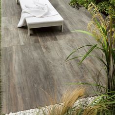 a white bed sitting on top of a wooden floor next to green plants and trees