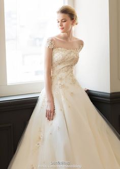 a woman in a wedding dress standing by a window with her hand on her hip