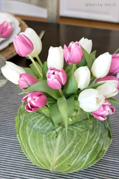 pink and white tulips in a green vase on a table with other flowers