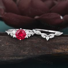 an engagement ring with a red stone surrounded by white diamonds on a piece of wood