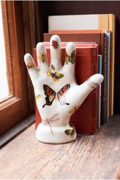 a ceramic hand with butterflies painted on it sitting next to a red book in front of a window