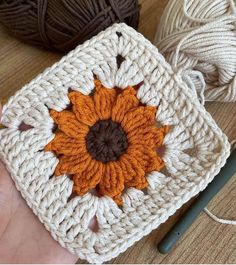 a crochet square with a sunflower on it and yarn balls in the background