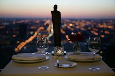 the table is set with wine glasses, plates and utensils in front of a cityscape