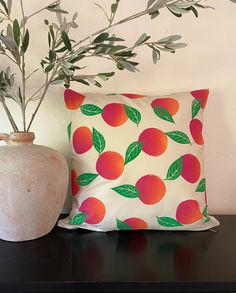 a vase and pillow sitting next to each other on a table with a plant in it