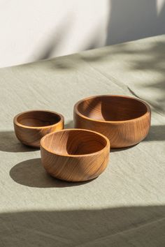 three wooden bowls sitting on top of a table next to a shadow from the sun