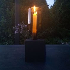 a lit candle sitting on top of a black block in the middle of a garden