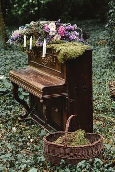 an old piano in the woods with flowers on top and candles lit next to it