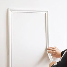 a person holding onto a white frame on the wall