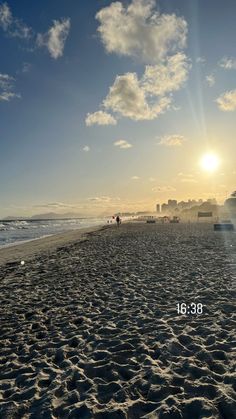 the sun is setting at the beach with people walking on it