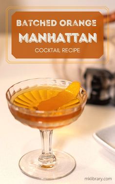 an orange manhattan cocktail in a coupe glass on a kitchen counter with the words, batched orange manhattan cocktail recipe