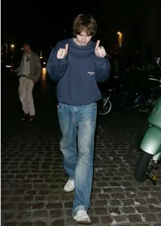 a young man walking down a street giving the thumbs up sign with his right hand