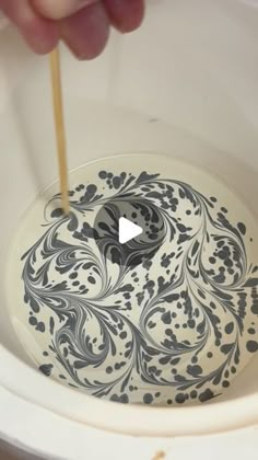 a person is stirring something in a white bowl with black and white designs on it