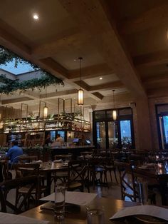 an empty restaurant with tables and chairs in front of large windows at night, while people are eating