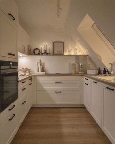 an attic kitchen with white cabinets and wood flooring on the walls is lit by recessed lighting