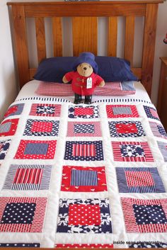 a teddy bear sitting on top of a bed with red, white and blue quilt