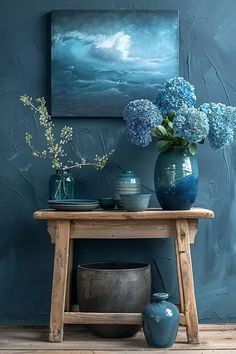 blue vases and flowers sit on a wooden table in front of a large painting