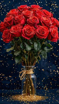 a bouquet of red roses in a glass vase with gold flakes on the table