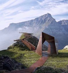 a wooden structure sitting on top of a lush green hillside next to a mountain range