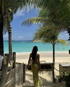 a woman in a yellow dress is walking on the beach with palm trees and blue water