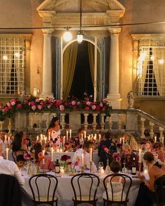 a group of people sitting around a table with candles in front of them and flowers on the wall