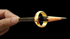 a person holding a pen with a gold ring on it's tip and an arrow in the middle