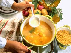 a person pouring soup into a pot on top of a stove next to other dishes