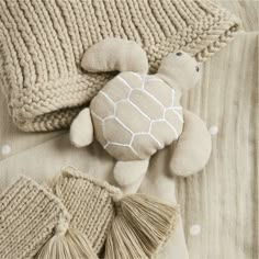 a stuffed turtle laying on top of a bed next to pillows and blankets with tassels