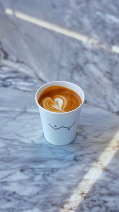 a cup of coffee with a heart drawn on the foam in it sitting on a marble table