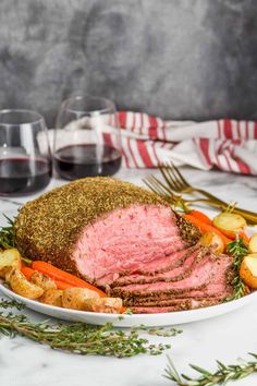 a plate with roast beef, potatoes and carrots next to two glasses of red wine