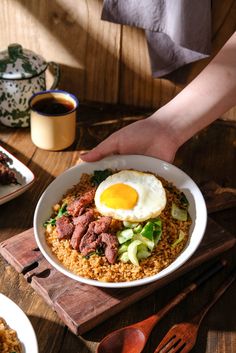 a person is reaching for an egg on top of rice with meat and veggies