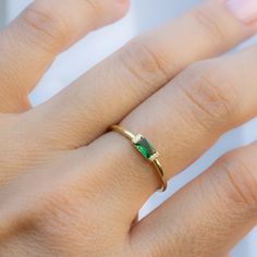 a woman's hand wearing a gold ring with an emerald stone in the middle