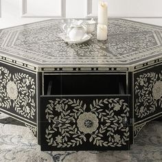 a black and white coffee table with an intricate design on the top, next to a lit candle