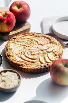 an apple pie is on a table with apples and other food items around the cake