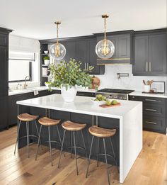 a kitchen with black cabinets and white countertops, two pendant lights over the island