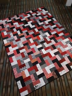 a red, black and white quilt is laying on a wooden floor next to a door