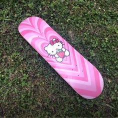 a pink skateboard with a hello kitty design on it laying in the green grass