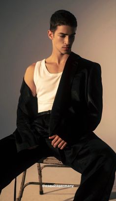 a man sitting on top of a chair wearing a white shirt and black suit jacket