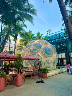 people sitting at tables under umbrellas in front of a large bubble like structure with round windows