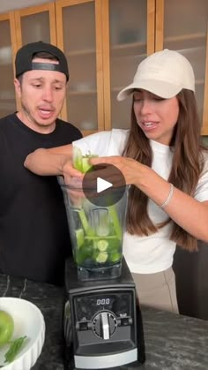 a man and woman are making green fruit in a blender with the help of an appliance