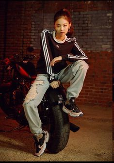 a woman sitting on top of a motorcycle in front of a brick wall and wearing ripped jeans