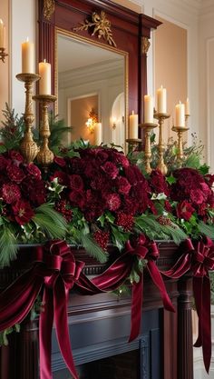 a mantel decorated with red flowers, greenery and candles