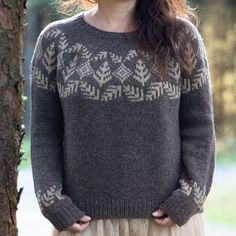 a woman standing in front of a tree with her hands on her hips wearing a sweater