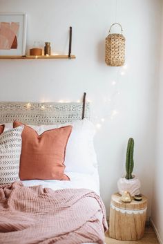 a white bed with pink pillows and blankets on top of it next to a potted cactus