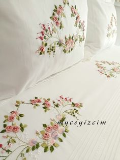 a white bed topped with lots of pillows and blankets covered in embroidered flowers on them