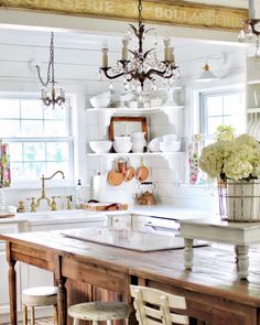 a kitchen with a wooden table and white cabinets, chandelier above the sink