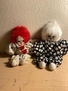 two clown dolls sitting next to each other on a wooden table with a white wall behind them