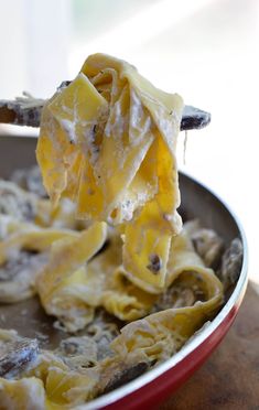 a spoon full of pasta and cheese being lifted from a red dish with it's fork