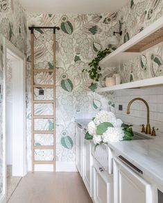 a kitchen with white cabinets and green wallpaper on the walls next to a ladder