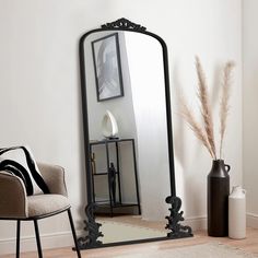 a large mirror sitting on top of a wooden floor next to a chair and vase